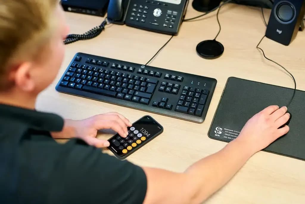 Medewerker van Verdo Loont berekent iets op zijn telefoon achter zijn bureau
